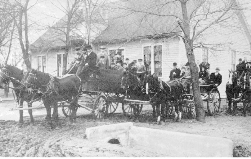The original East Prairie school behind several wagonloads of parents and children